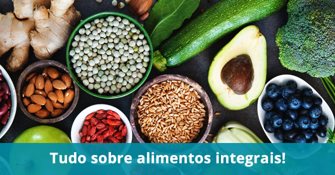 Fotografia com vários alimentos integrais como abacate, brócolis, pepino, sementes, frutas e gengibre.